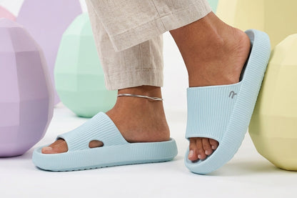 Light blue sandals worn with beige pants against a colorful background