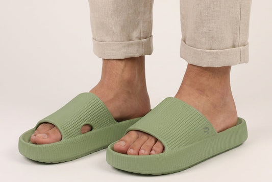 Green slides worn with beige pants on a plain background